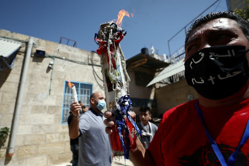 An Orthodox Christian worshipper wears a face mask and holds candles-stick with fire following The Holy Fire ceremony that took place in the Church of the Holy Sepulchre in Jerusalem's Old City amid the coronavirus disease (COVID-19) outbreak