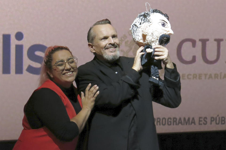 Una fan le regala una piñata al cantante y actor español Miguel Bosé, derecha, durante una charla sobre la película "Tacones lejanos" en el Festival Internacional de Cine de Morelia en Morelia, México, el lunes 23 de octubre de 2023. (Foto AP/Berenice Bautista)