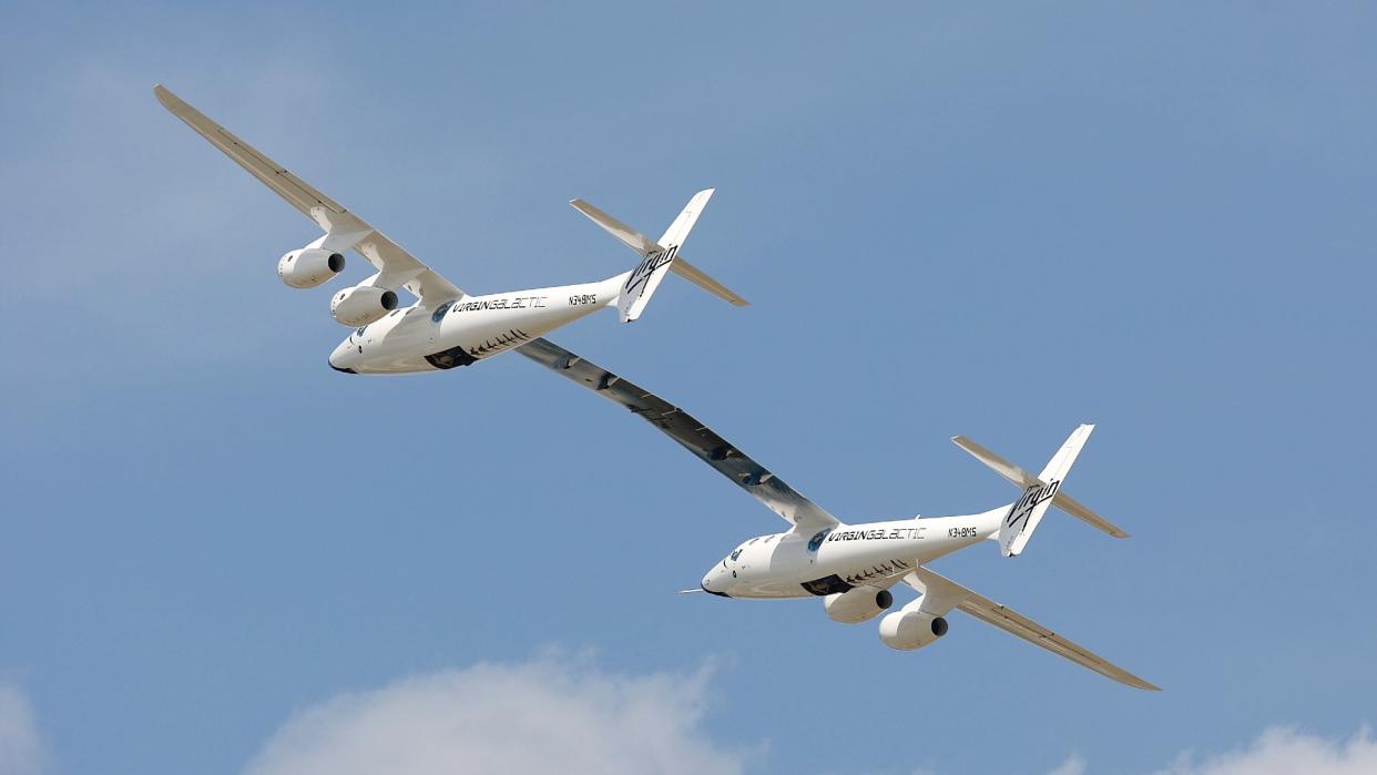  Two white aircraft joined together as one at the wing fly through a blue sky. 