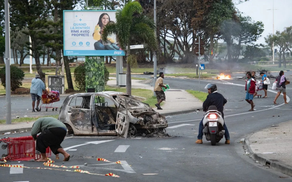 A burnt-out car, and various people with shopping trolleys