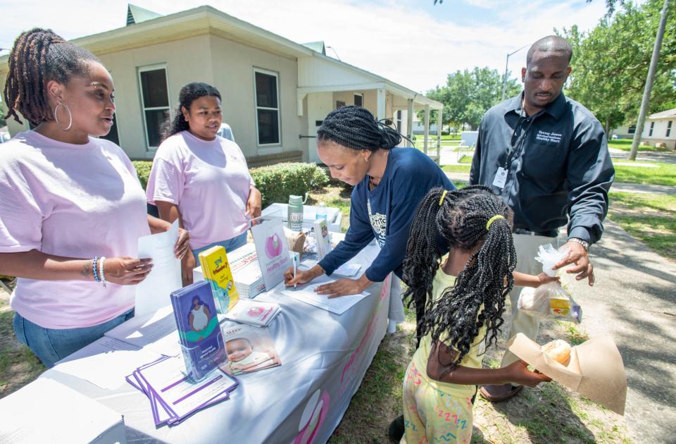 From left, Escambia County Healthy Start Coalition community liason Lakeila Robertson and projects coordinator Jade Christian help Ariel Cook fill out paperwork as Cariel Cook, 6, gets a lunch from fatherhood coordinator Torrey Jones during an outreach event at Attucks Court in Pensacola on Monday, June 26, 2023.