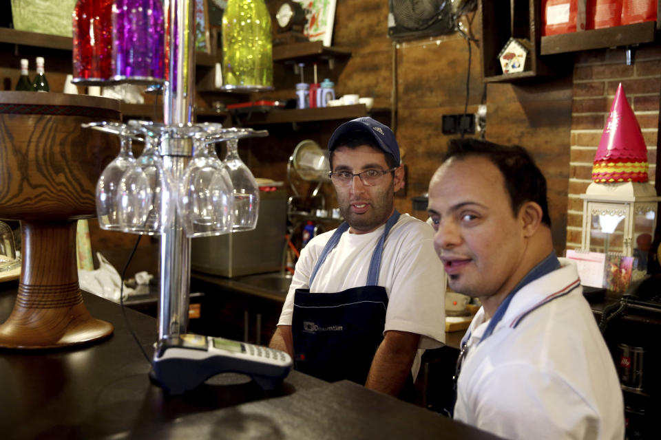 In this Monday, Aug. 6, 2018, photo, two cafe staffers, Mehdi Khakian, with autism, left, and his colleague Iman Arbabi, with down syndrome, work in Downtism Cafe in Tehran, Iran. The popular cafe, whose name combines “Down” with “autism,” in Tehran’s bustling Vanak Square is entirely run by people with Down syndrome or autism. More than just providing meaningful work, the cafe is helping break down barriers by highlighting how capable people with disabilities are. (AP Photo/Ebrahim Noroozi)