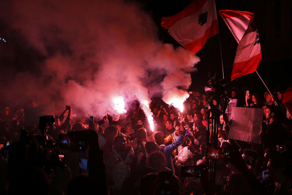 Protesters hold flares and Lebanese flags, during ongoing protests against the Lebanese government, in front of the Central Bank, in Beirut, Lebanon, Thursday, Nov. 28, 2019. Lebanon paid back a Eurobond worth $1.5 billion that was scheduled to mature Thursday, a Finance Ministry official said, pacifying concerns of a first-ever default on its debt amid the worst financial crisis in three decades. (AP Photo/Bilal Hussein)