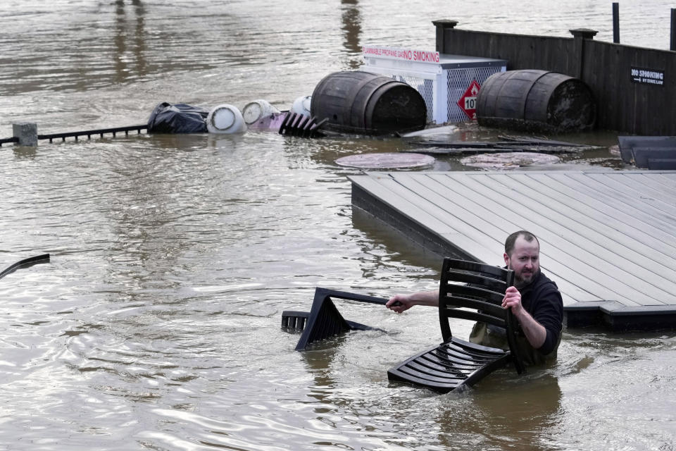 FILE - Nathan Sennett, a cook at the Quarry Tap Room, wades through flood water to retrieve furniture from the restaurant's patio near the Kennebec River, Tuesday, Dec. 19, 2023, in Hallowell, Maine. Unseasonably warm weather, including rain storms in the northeast, is washing away snow at ski areas and reducing the chances that many people in the U.S. will experience a white Christmas this year. (AP Photo/Robert F. Bukaty, File)