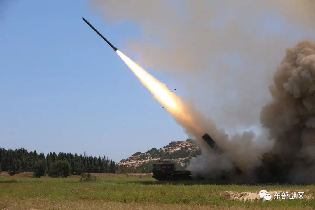 Missile being launched from grassy field near trees and hills.