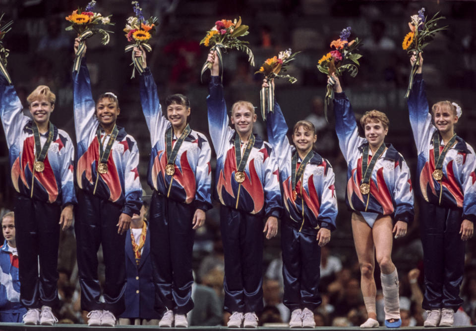 ATLANTA - JULY 23:   The United States Women's Gymnastics Team (L-R) of Amanda Borden, Dominique Dawes, Amy Chow, Jaycie Phelps, Dominique Moceanu, Kerri Strug, and Shannon Miller salutes the crowd after receiving their gold medals in the Team competition of the 1996 Summer Olympic Games held on July 23, 1996 in the Georgia Dome in Atlanta, Georgia.  The USA Women's team was nicknamed the Magnificent Seven.  (Photo by David Madison/Getty Images)