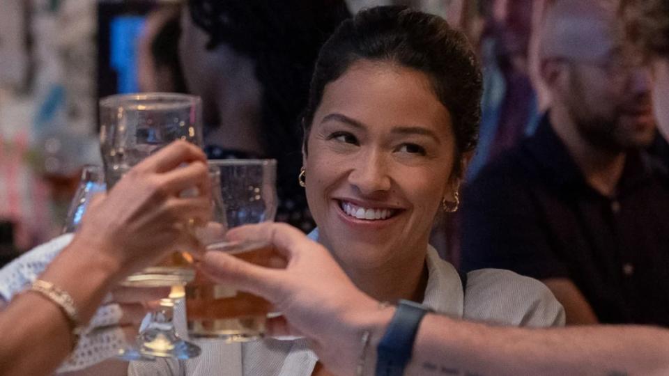 Gina Rodriguez smiles and raises a glass to cheers in a still image from Netflix's Players