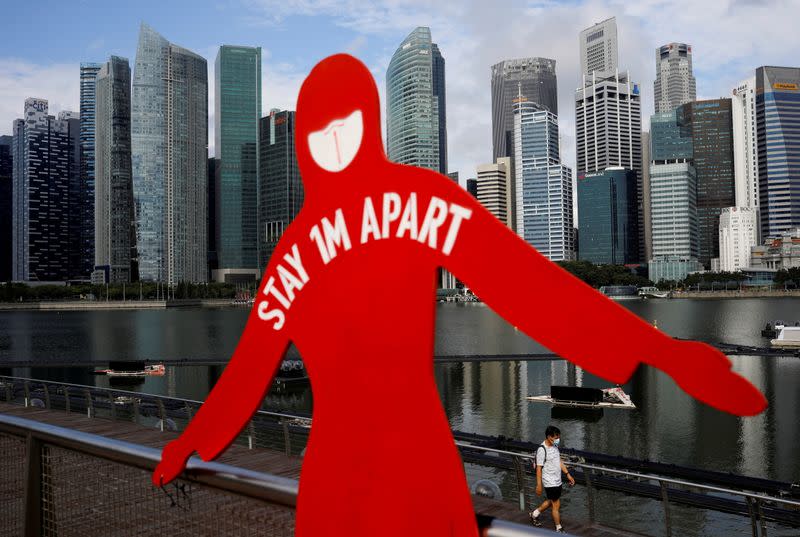 A man wearing a face mask passes a sign put up to encourage social distancing during the coronavirus disease (COVID-19) outbreak, at Marina Bay in Singapore