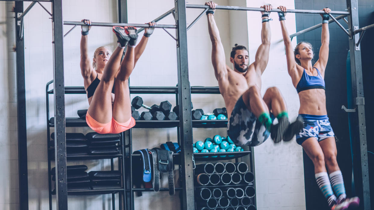  Three people performing toes-to-bar exercise in the gym. 