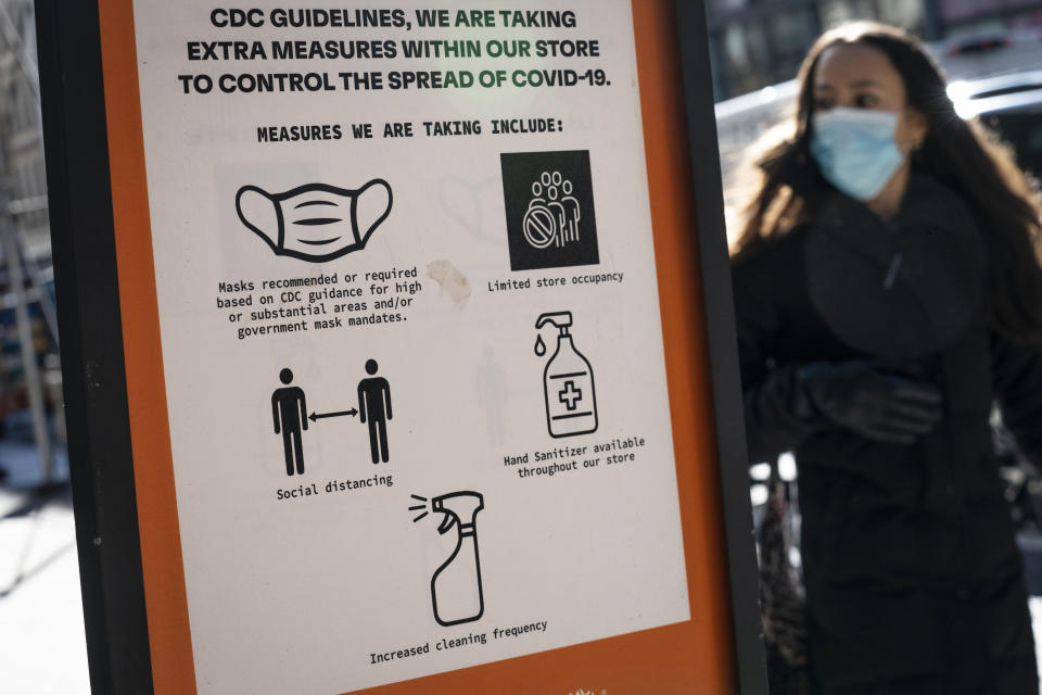 A person wearing a mask walks by a sign in New York City outlining the CDC’s guidelines to control the spread of COVID. 