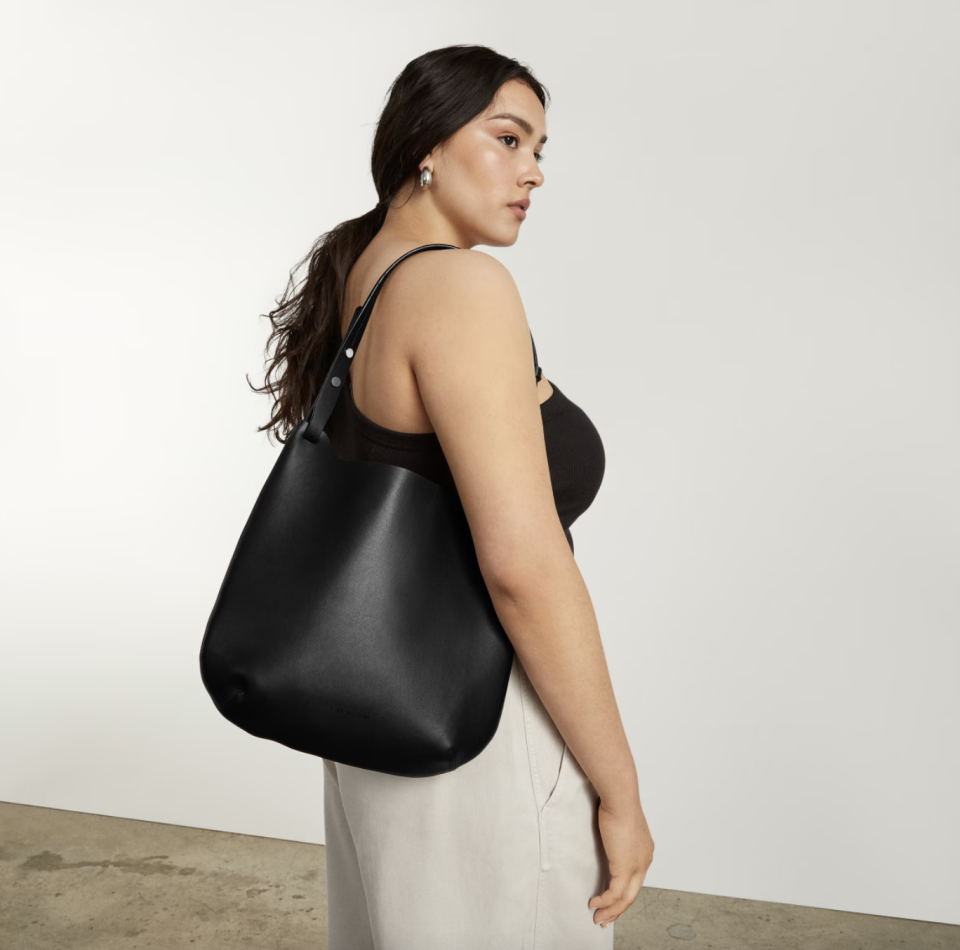 model with black hair wearing black tank top, white pants, and black bag, The Cactus Leather Hobo in Black (Photo via Everlane)