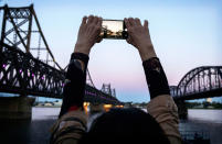 <p>A Chinese tourist takes pictures between “Friendship Bridge”, left, and “Broken Bridge”, right, as she looks across the Yalu river from the border city of Dandong, Liaoning province, northern China towards the city of Sinuiju, North Korea on May 23, 2017 in Dandong, China. (Photo: Kevin Frayer/Getty Images) </p>