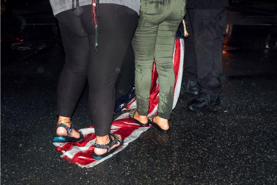 Two women stand on an American flag that throughout the day had been hung at various locations by a man aiming to call attention to racial injustices.