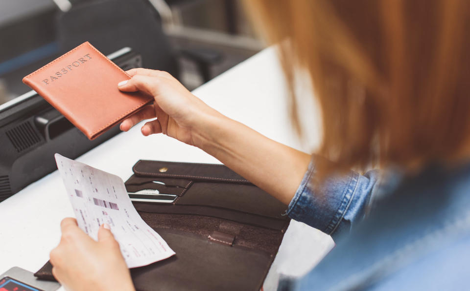 Young female passenger is giving her passport to check-in officer. Close up of her hands holding flight ticket