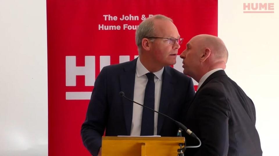 Simon Coveney is ushered from the room at The Houben Centre (Hume Foundation/PA) (PA Media)