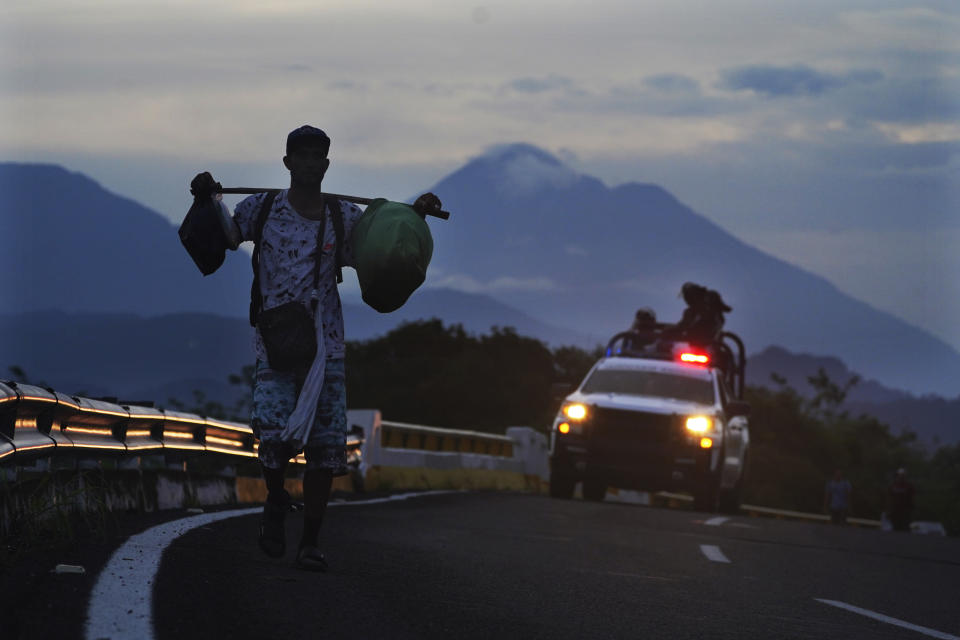 A migrant walks on the highway, followed by a Mexican National Guard vehicle, toward the exit to Huixtla, Chiapas state, Mexico, at sunrise Thursday, June 9, 2022. A group of migrants left Tapachula on Monday, tired of waiting to normalize their status in a region with little work, with the ultimate goal of reaching the U.S. Behind is the Tacana volcano. (AP Photo/Marco Ugarte)