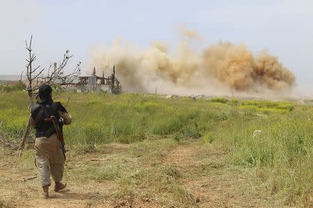 An Islamist rebel fighter walks as smoke rises after what activists said was an air strike by forces of Syria's President Bashar al-Assad at Qarmeed camp, after Islamist rebel fighters took control of the area April 27, 2015. REUTERS/Ammar Abdullah