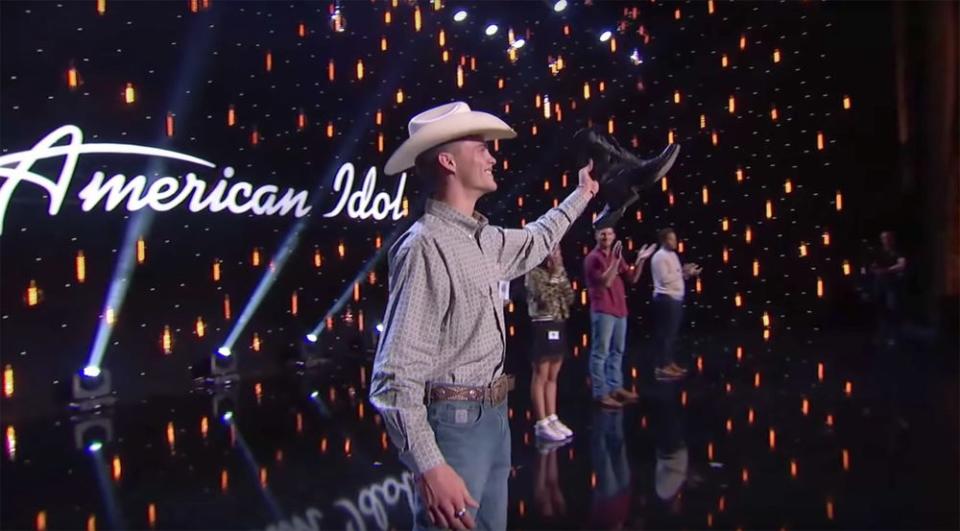 Colby Swift proudly holds up the boots Luke Bryan gave to him