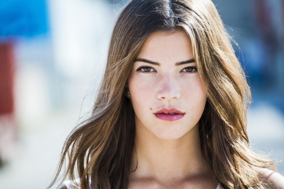 Woman with brown hair and facial mole staring into the camera.