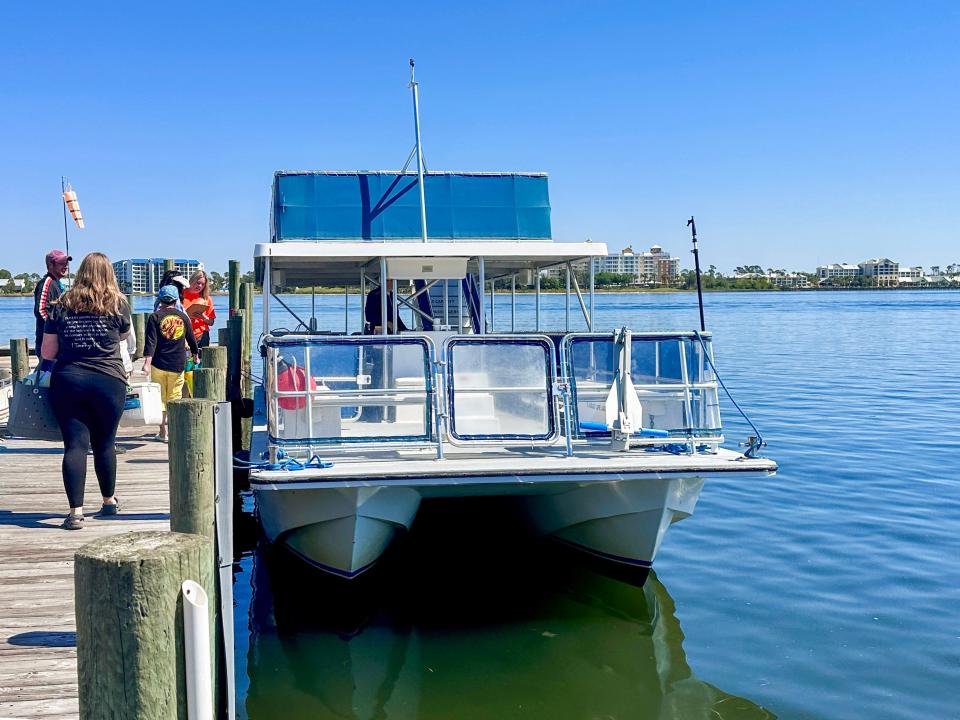 A dock with people boarding a ferry. The ferry is mostly white with blue detailing and sits in blue-green water