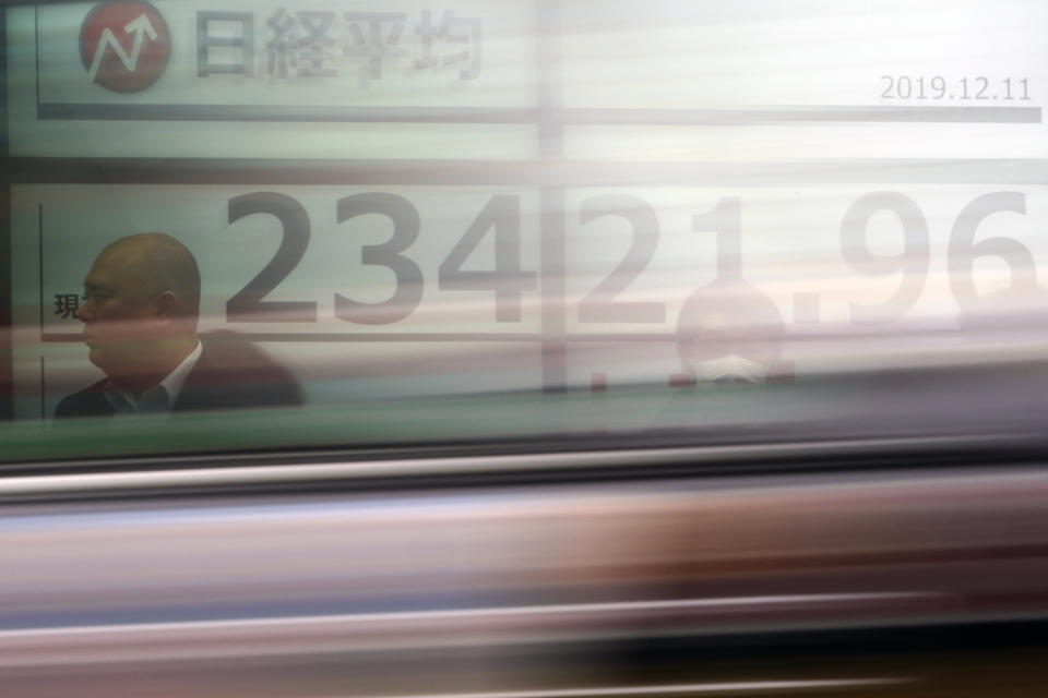 A car passes by people standing near an electronic stock board showing Japan's Nikkei 225 index at a securities firm in Tokyo Wednesday, Dec. 11, 2019. (AP Photo/Eugene Hoshiko)