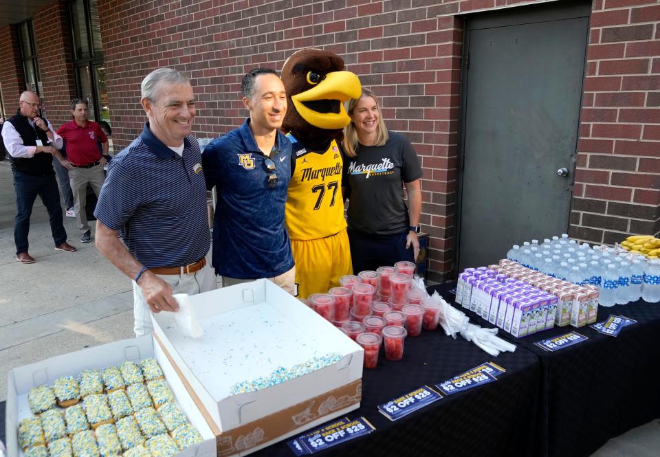 Marquette University president Michael Lovell, men's basketball coach Shaka Smart, the Marquette University mascot, Iggy, and women's basketball coach Megan Duffy, pose for a photo while handing out free breakfasts at Sendik's Fresh2Go on the Marquette campus.