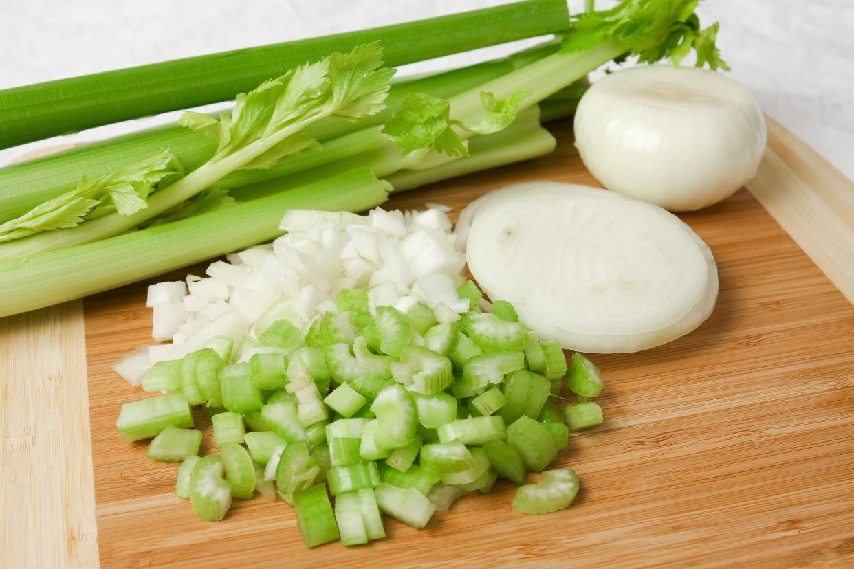 Chopped, sliced and whole celery and onion on a wooden cutting board.