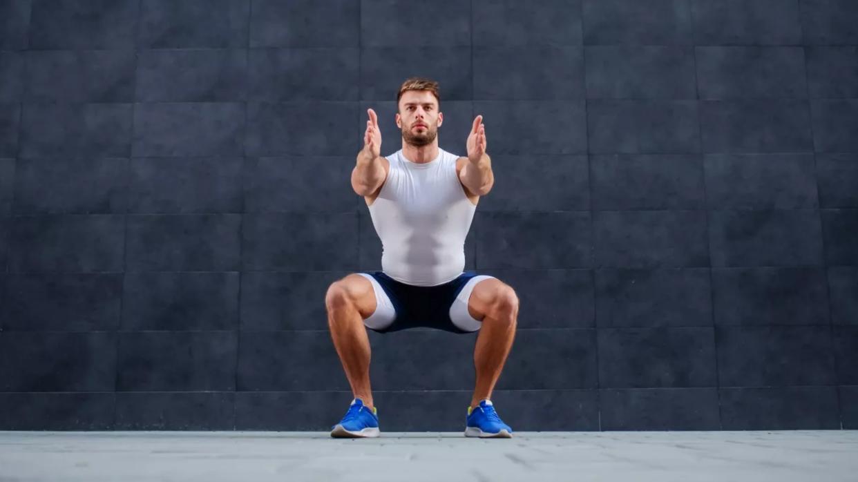  Man performing a squat face on against a grey background outside 
