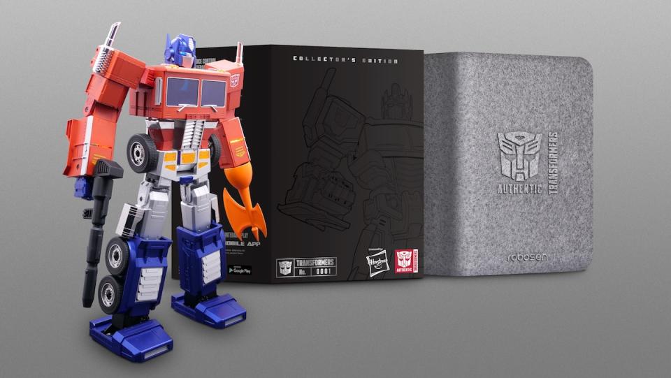 An Optimus Prime Toy Robot standing next to boxes it comes packaged in