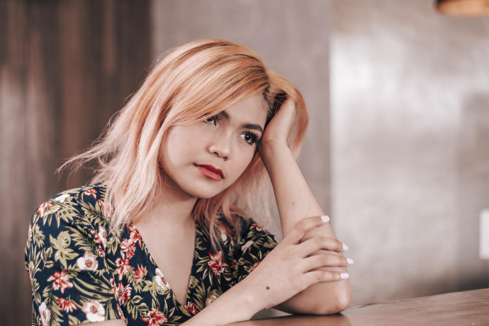 Person sitting at a table looking pensive with a hand on head, wearing a floral shirt