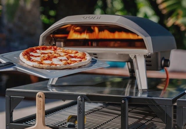 the dome shaped outdoor pizza oven with a pizza being slid into it