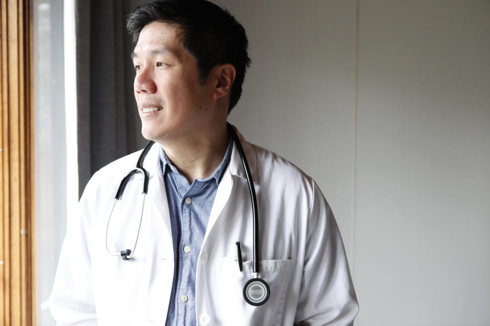 Doctor in white coat with stethoscope looking out window, conveying thoughtfulness