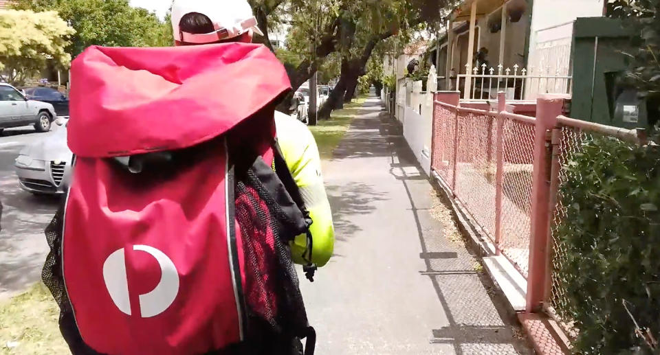 Postie walking down street delivering mail.