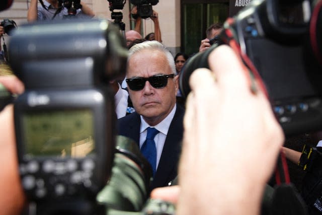 Huw Edwards, wearing sunglasses, surrounded by photographers as he leaves court