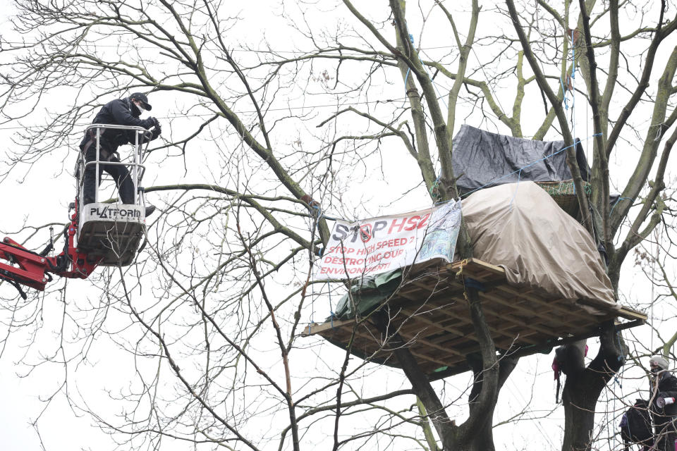 A cherry picker approaches an HS2 Rebellion treetop camp in an encampment in Euston Square Gardens in central London,, Wednesday Jan. 27, 2021. Protesters against a high-speed rail link between London and the north of England said Wednesday that some of them have been evicted from a park in the capital after they dug tunnels and set up a makeshift camp. (Aaron Chown/PA via AP)