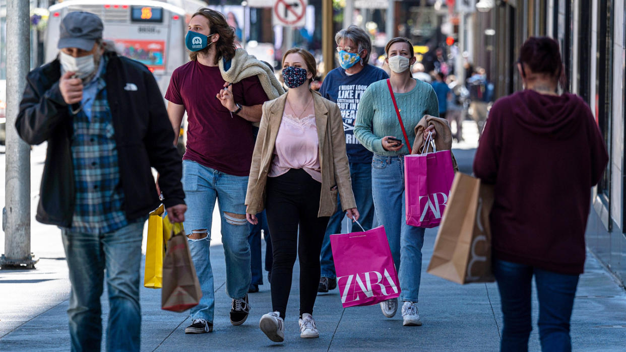 People on a sidewalk wearing protective masks and carry shopping bags