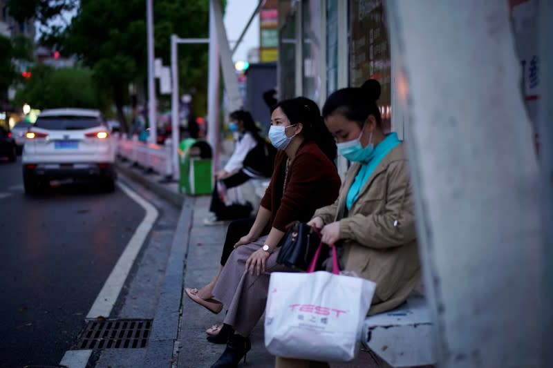 Women wearing face masks wait for buses at a bus stop in Xianning