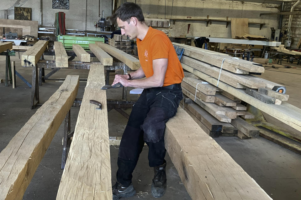 French framer Brieuc de Keranflec'h works on a beam, part of the new roof of Notre Dame de Paris cathedral, Thursday, May, 25, 2023, near Angers, western France. Carpenters building a new timber frame for the fire-ravaged roof of Paris' Notre Dame Cathedral are using the same tools and techniques as their medieval predecessors. For them, working with hand-axes to fashion oak beams has been like stepping back in time. (AP Photo/Jeffrey Schaeffer)