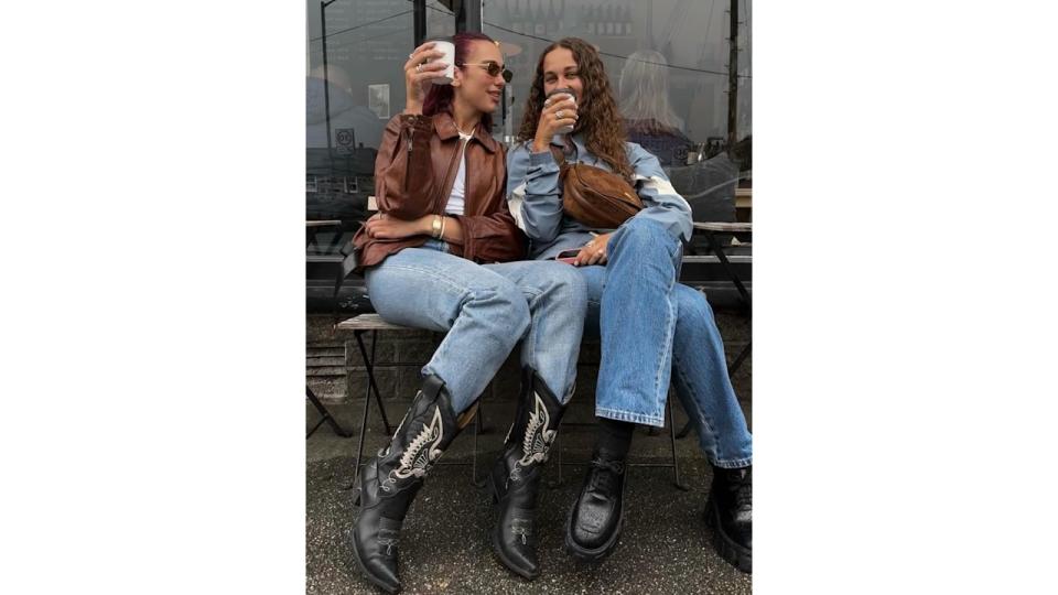 Dua Lipa and Sarah Lysander pose on a bench with coffees