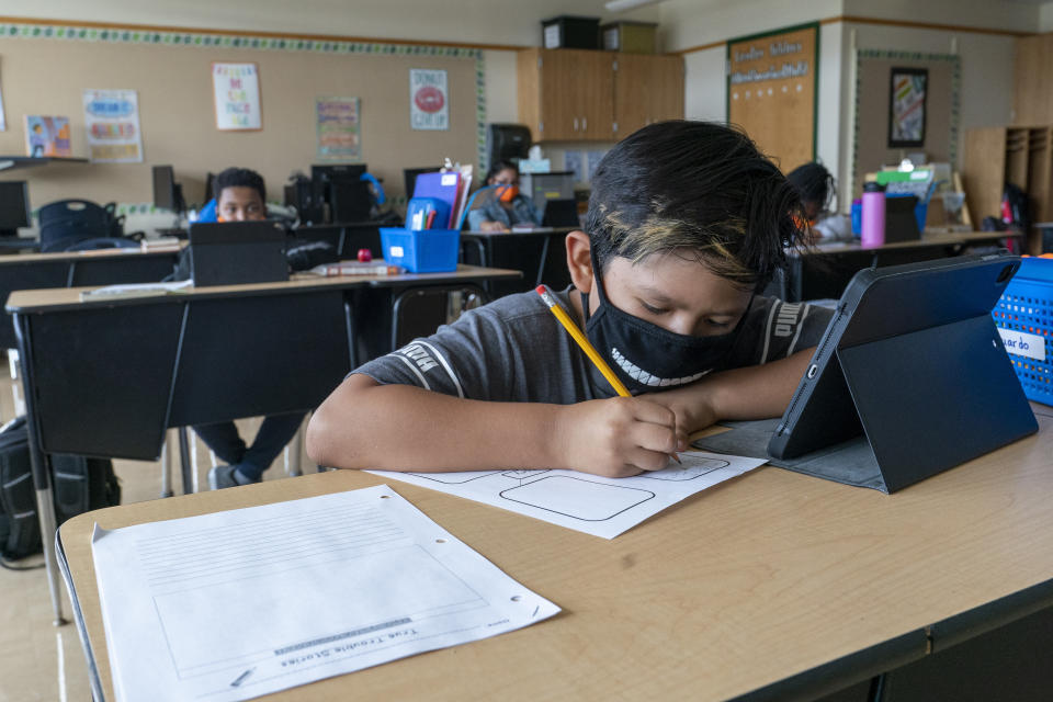 FILE - A student wears a face mask while doing work at his desk at the Post Road Elementary School, in White Plains, N.Y., in this Thursday, Oct. 1, 2020, file photo. U.S. health officials say the highly contagious delta version of the coronavirus is behind changes to mask guidelines. The Centers for Disease Control and Prevention this week announced that fully vaccinated people should resume wearing masks indoors if they live in areas where the virus is surging. CDC officials said new information about the spread of the delta variant forced them to reverse course. The agency also said teachers and students everywhere should go back to wearing masks in schools. (AP Photo/Mary Altaffer, FIle)