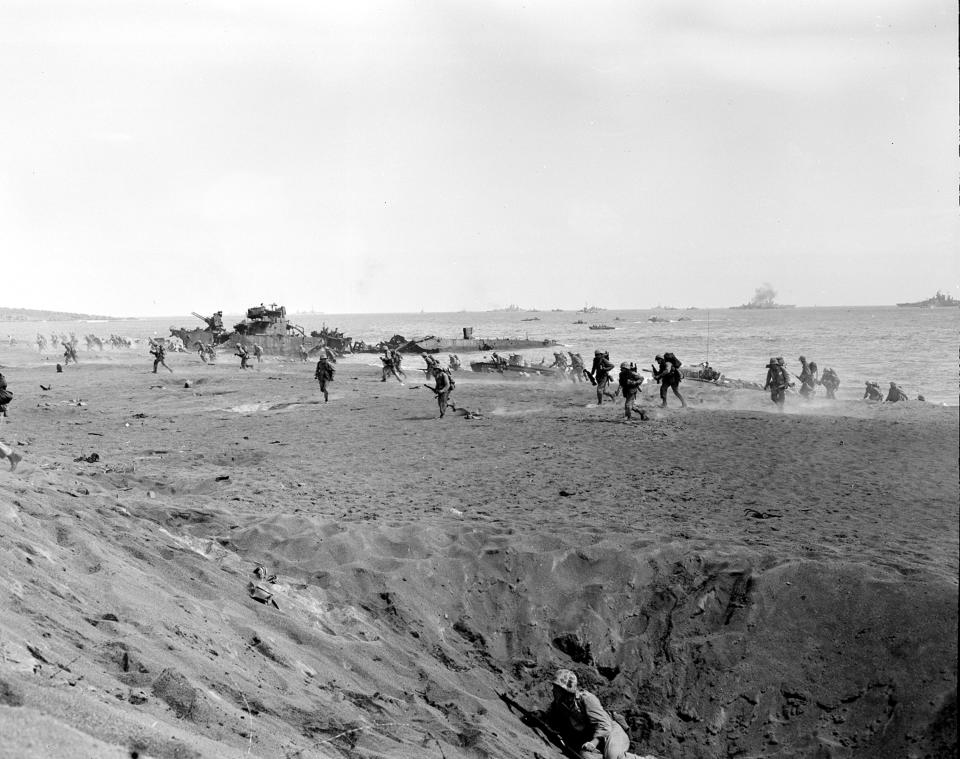 U.S. Marines of the 4th Division charge ashore at the start of the Iwo Jima invasion, running for cover in shell holes and bomb craters made by pre-invasion bombardments, on Feb. 25, 1945, during World War II. Warships offshore gave heavy gun support.