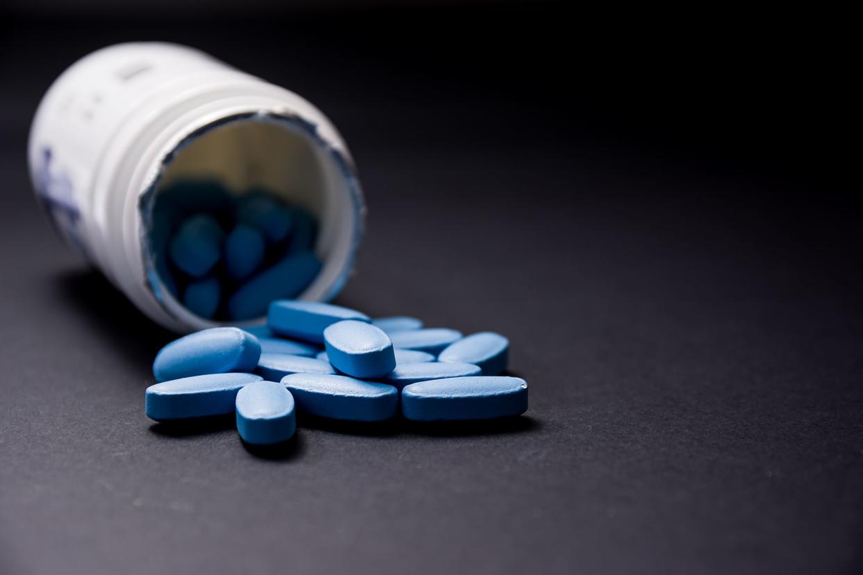 Blue pills in the foreground come out of the white plastic container in the blurred background