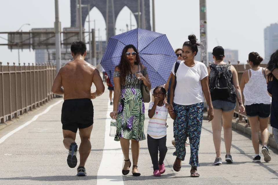 A woman carries an umbrella to shade herself from the heat as a jogger passes by on the Brooklyn Bridge, Wednesday, Aug. 29, 2018, in New York. The National Weather Service says temperatures in the 90s combined with high humidity are pushing the heat index past 100. (AP Photo/Mark Lennihan)