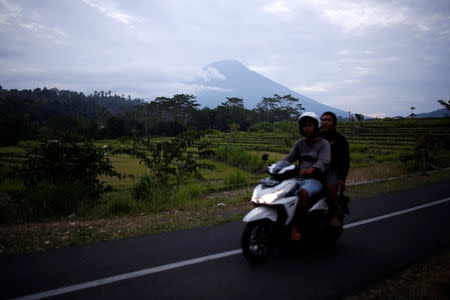 People ride a motorcycle past Mount Agung in the background, a volcano on the highest alert level, in Karangasem Regency, on the resort island of Bali, Indonesia, September 24, 2017. REUTERS/Darren Whiteside