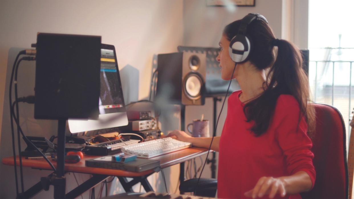  A woman sits at a desk making music on a computer. 