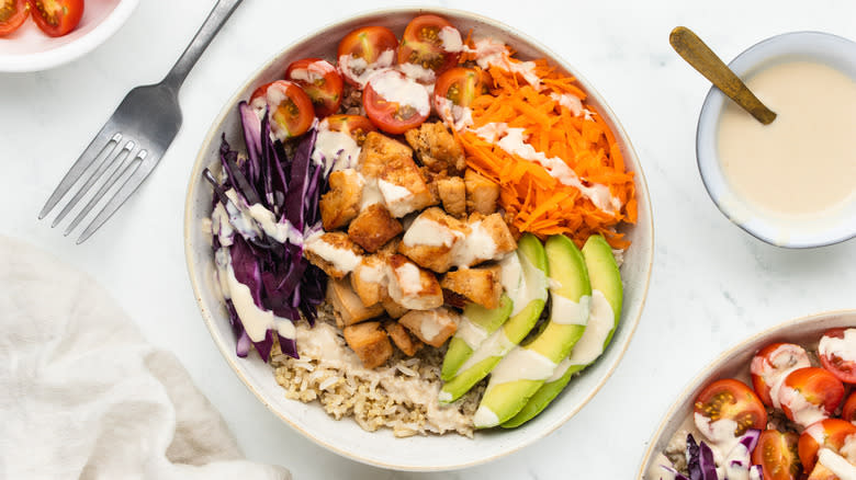 A bowl of tofu, salad and grains with dressing