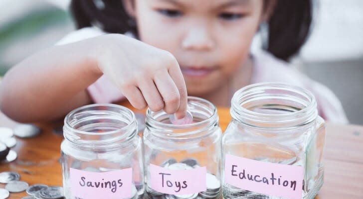 Image shows a child sitting in front of three jars with coins in each; the jars are labeled &quot;Savings,&quot; &quot;Toys&quot; and &quot;Education.&quot;