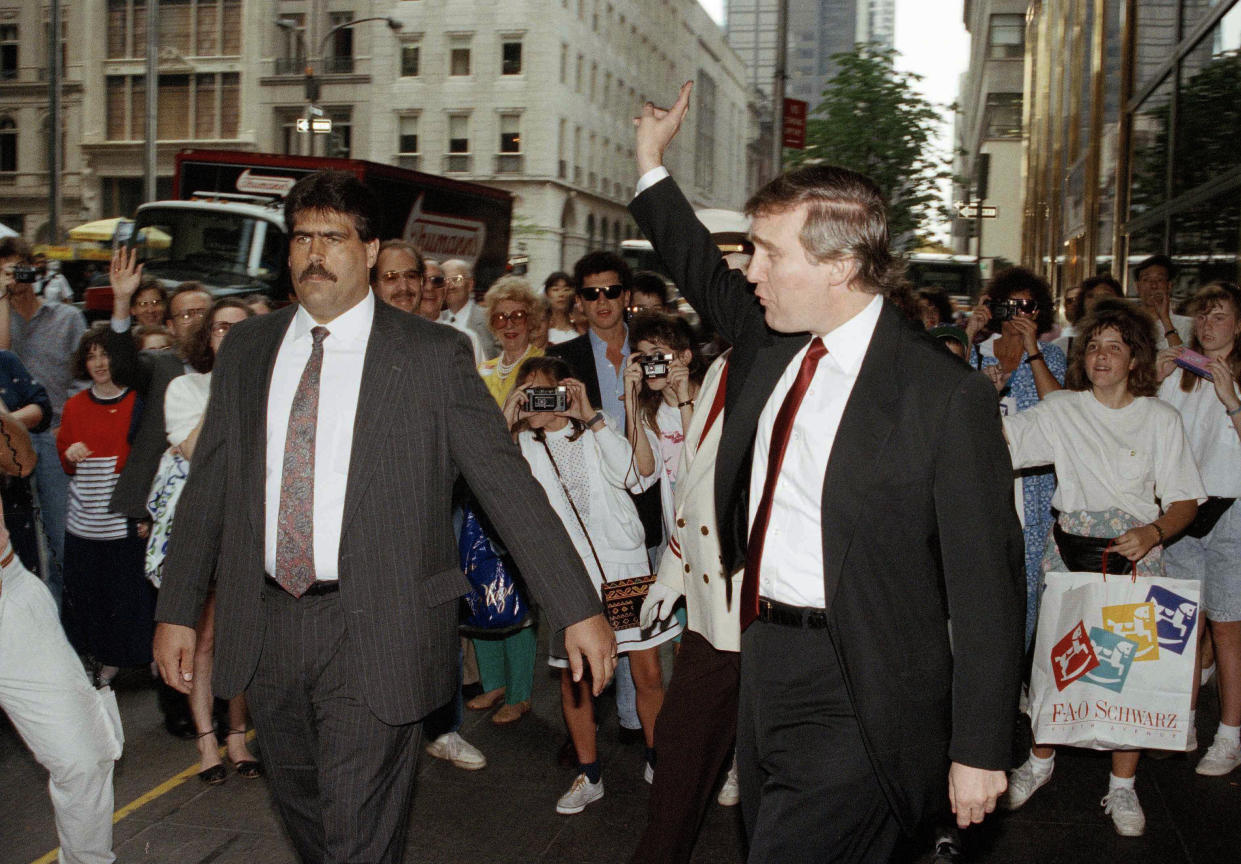 FILE - Donald Trump, right, waves to onlookers while leaving his residence at Trump Tower in New York, June 8, 1990. Trump tried unsuccessfully to evade the press amid recent reports of his financial troubles. The man at left is unidentified. (AP Photo/Mario Suriani, File)