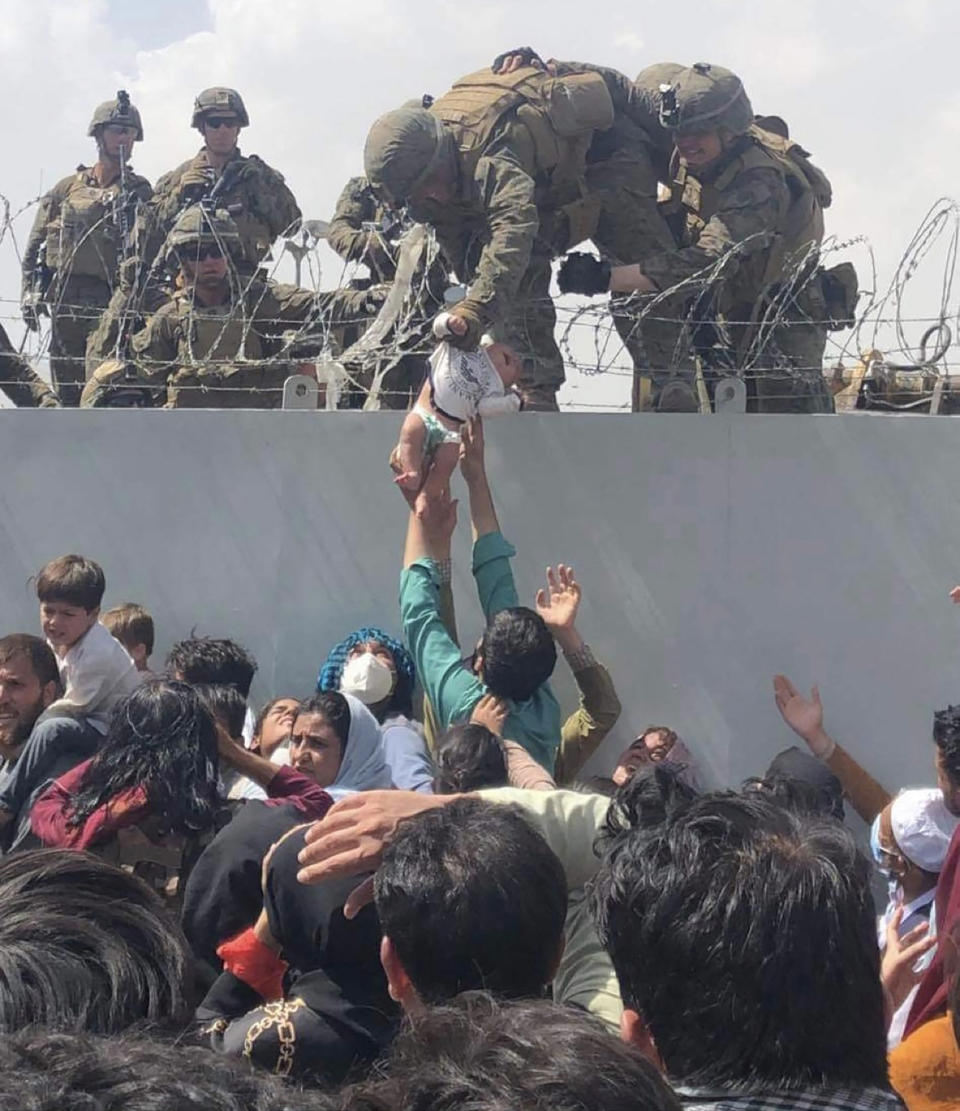 TOPSHOT - This image made available to AFP on August 20, 2021 by Omar Haidiri, shows a US Marine grabbing an infant over a fence of barbed wire during an evacuation at Hamid Karzai International Airport in Kabul on August 19, 2021. - A Pentagon official confirmed Friday that US evacuation operations from Kabul's airport have been stalling because the receiving base in Qatar is overflowing and could not receive evacuees. 