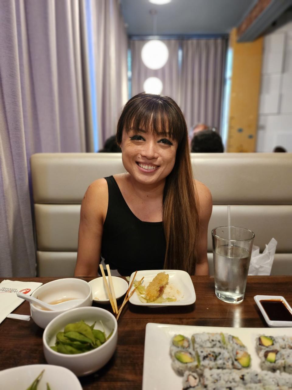 <p>A picture taken with the Galaxy Z Flip 4 showing a woman with light brown hair posing in front of some plates of food, including edamame, chicken tempura and sushi.</p>
